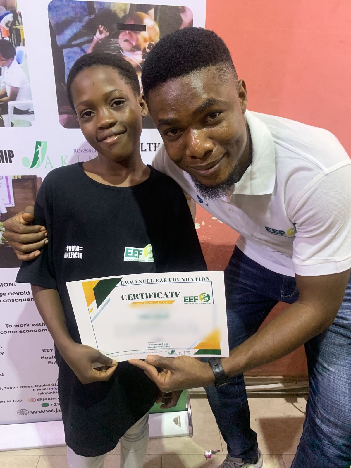 A student holding a computer training certificate beside a volunteer